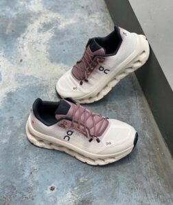 d0d189af-6bcc-479b-a182-4a288833e544 | UAE SPORT STORE Pair of white and dusty pink On running shoes with chunky beige soles and black inner lining resting on a blue-gray concrete floor.