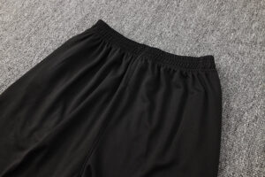 Black athletic pants with an elastic waistband laid flat on a gray carpet.