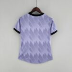 Lavender T-shirt with a zigzag pattern on a wooden hanger against a light wall.