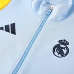 Close-up of a light-blue jacket zipper with visible stitching and a partial dark crest/logo at the bottom right