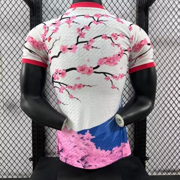 Back view of a white cycling jersey with pink cherry blossoms, red collar and sleeve cuffs, on a black mannequin.