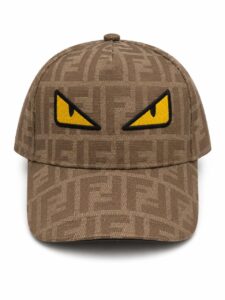 Brown patterned baseball cap with a bold yellow angry-eye patch on the front panel for a playful, edgy look.