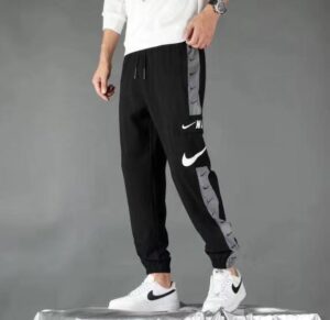 Person wearing black Nike joggers with gray side panels and white swoosh logos, paired with white Nike sneakers on a neutral backdrop.