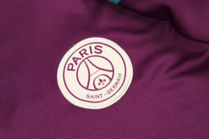 Embroidered Paris Saint‑Germain badge on a purple jersey or fabric surface studs.