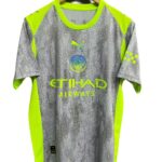 Manchester City away jersey on a wooden hanger, neon yellow and grey with a rain-drop pattern and sponsor logos (Etihad).