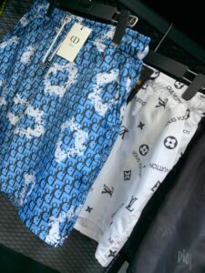 Blue Dior monogram patterned shorts hanging on a rack, next to white Louis Vuitton-branded shorts with logos on the fabric tag included.