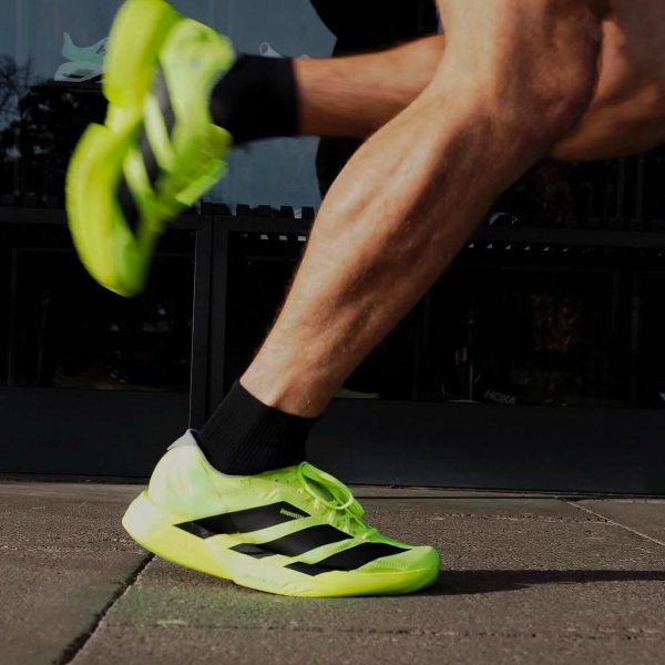 Neon yellow running shoe in mid-stride as a person lands on a pavement surface.