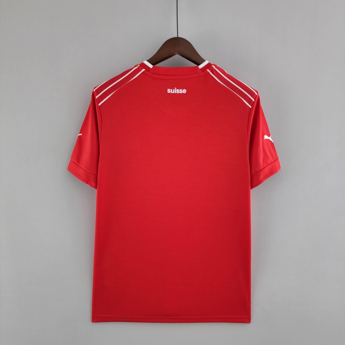 Red athletic jersey on a wooden hanger against a gray wall, with the word 'suisse' visible on the back collar area.