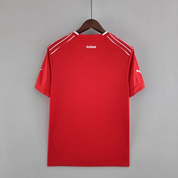 Red athletic jersey on a wooden hanger against a gray wall, with the word 'suisse' visible on the back collar area.