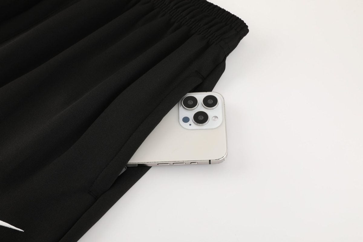 Silver iPhone with triple cameras resting on a white surface beside a black elasticated garment.