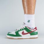 Low-top Nike sneaker in white, green, and red on a person wearing white socks with a visible calf.