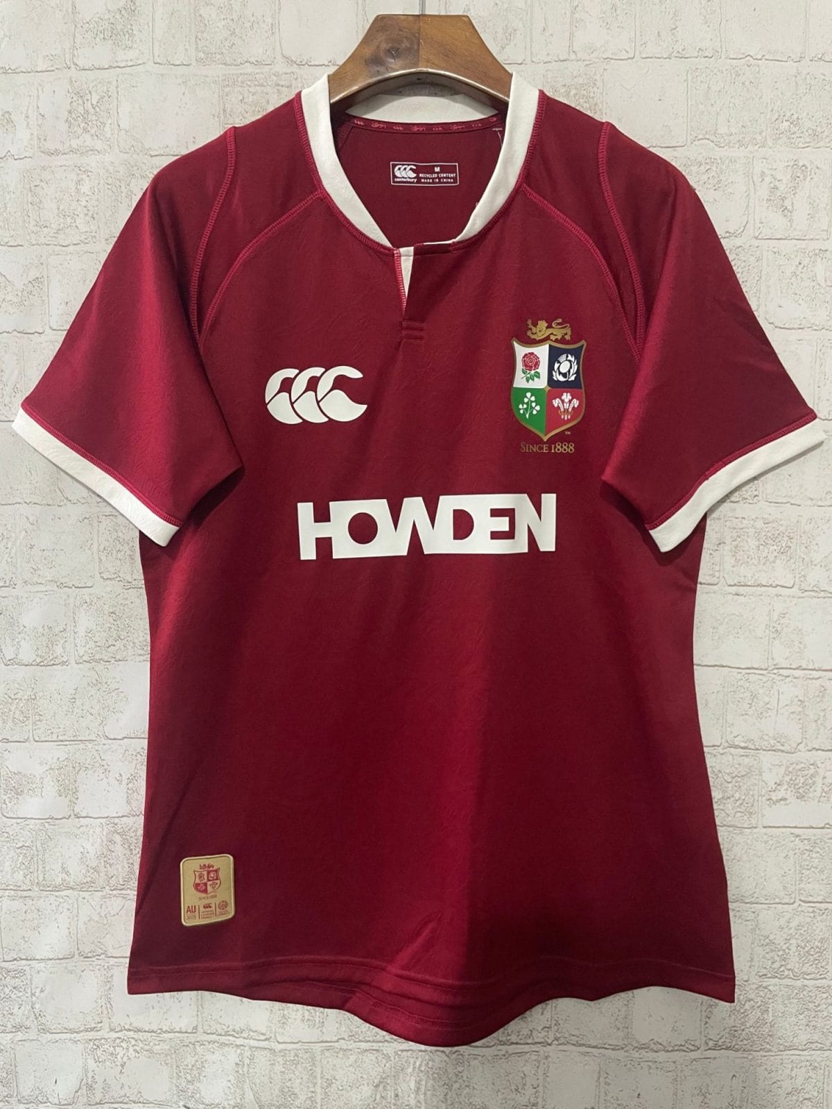 Maroon rugby jersey on hanger with white trim, featuring the Crest of four quadrants on the left chest and the 'HOWDEN' sponsor logo across the front. White polo-style collar with light trim.