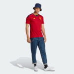 Model wearing a red Spain national team jersey, blue bucket hat, cuffed jeans, and white sneakers for a casual streetwear look.