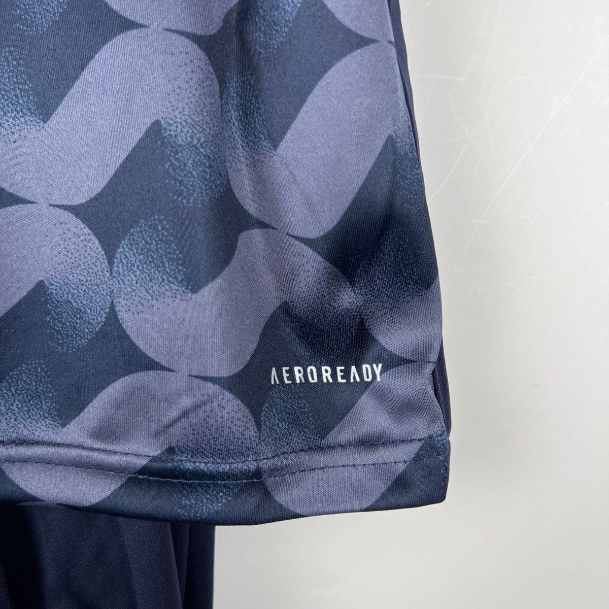 Close-up of dark blue camouflage fabric with visible AEROREADY branding on the edge of a garment pocket or seam