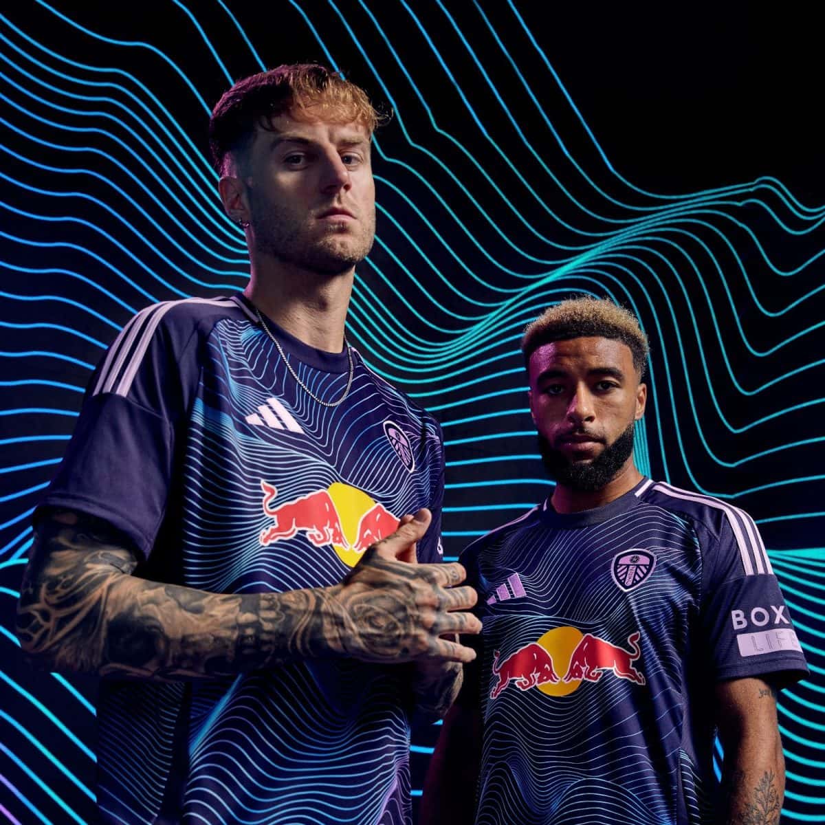 Two athletes in matching dark blue Red Bull team jerseys stand before a neon blue wavy-background.