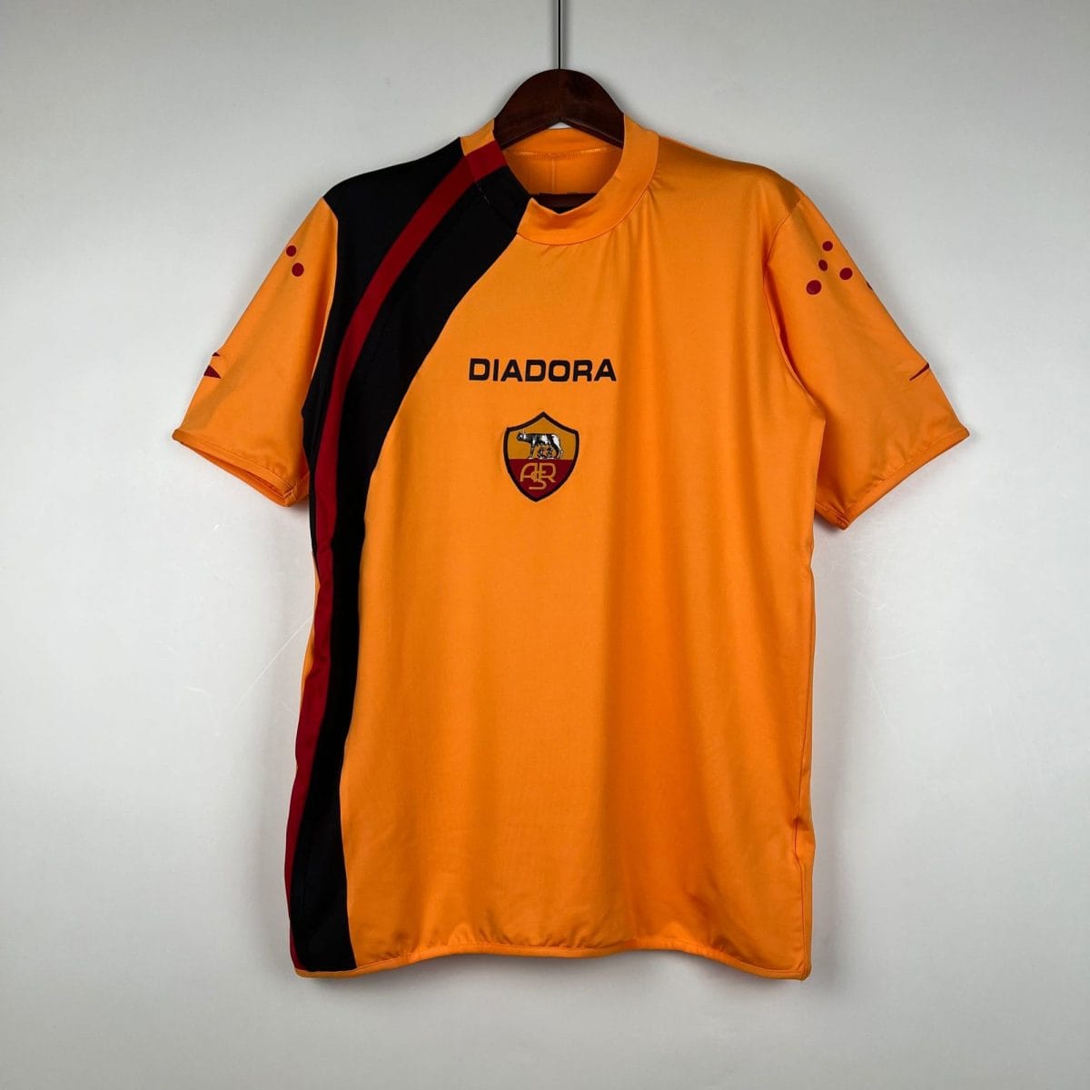Orange Diadora sports jersey on a hanger, featuring a black and red diagonal stripe and a team crest logo.