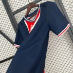 Navy blue varsity-style jacket on a wooden hanger, with white and red trim, displayed against a metal grid backdrop in a store setting.