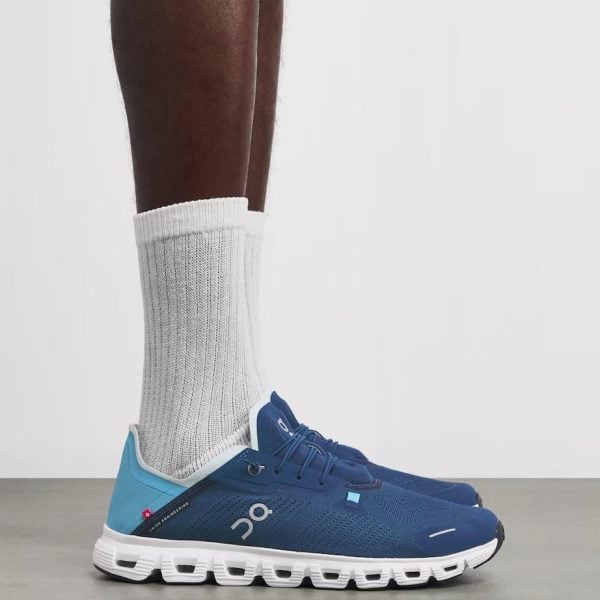 Blue running shoes with a white segmented sole, worn with white crew socks, side view.