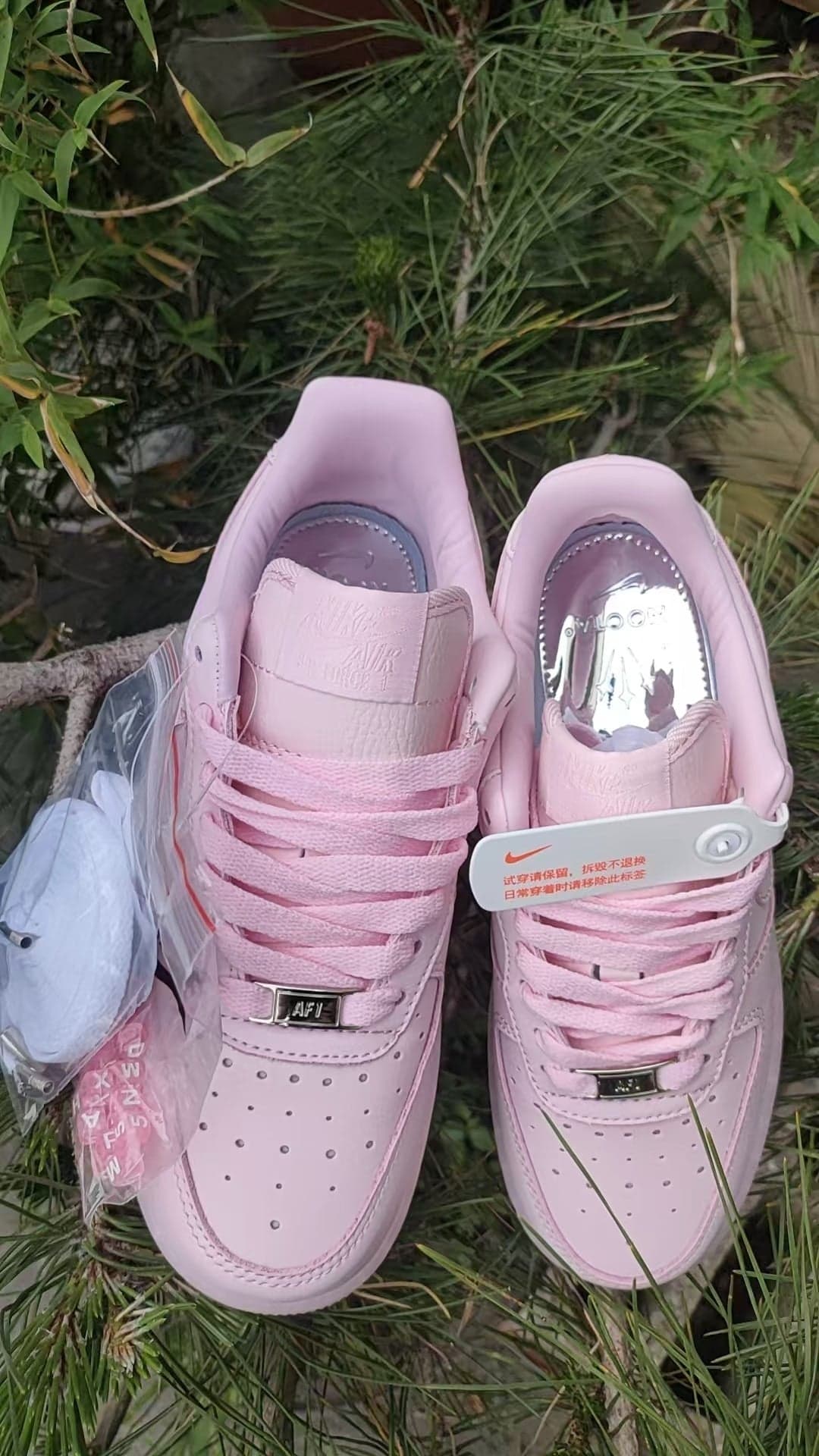 d4e249fc | UAE SPORT STORE Two light-pink Nike Air Force 1 sneakers with pink laces on grass, showing perforated toes and a white tag on the right shoe.