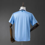 Back view of a light blue short-sleeve athletic jersey on a dress form, with a dark collar trim visible at the neck.
