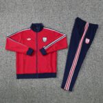 d5179b73 | UAE SPORT STORE Red Arsenal track jacket with navy cuffs and white stripes laid beside matching navy track pants on a gray carpet, outfit ready to wear.