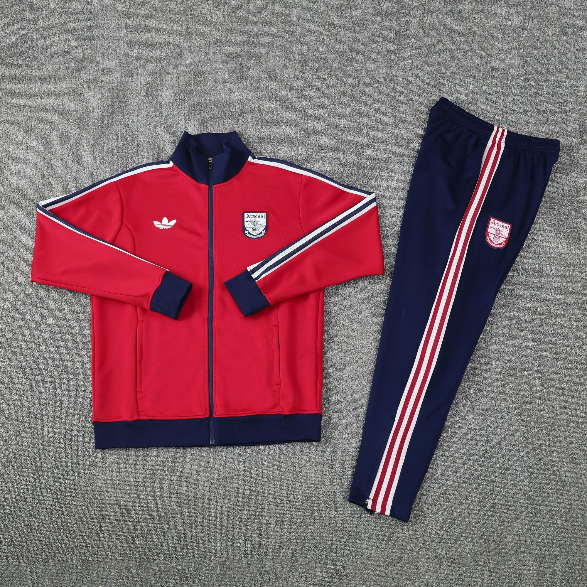 d5179b73 | UAE SPORT STORE Red Arsenal track jacket with navy cuffs and white stripes laid beside matching navy track pants on a gray carpet, outfit ready to wear.