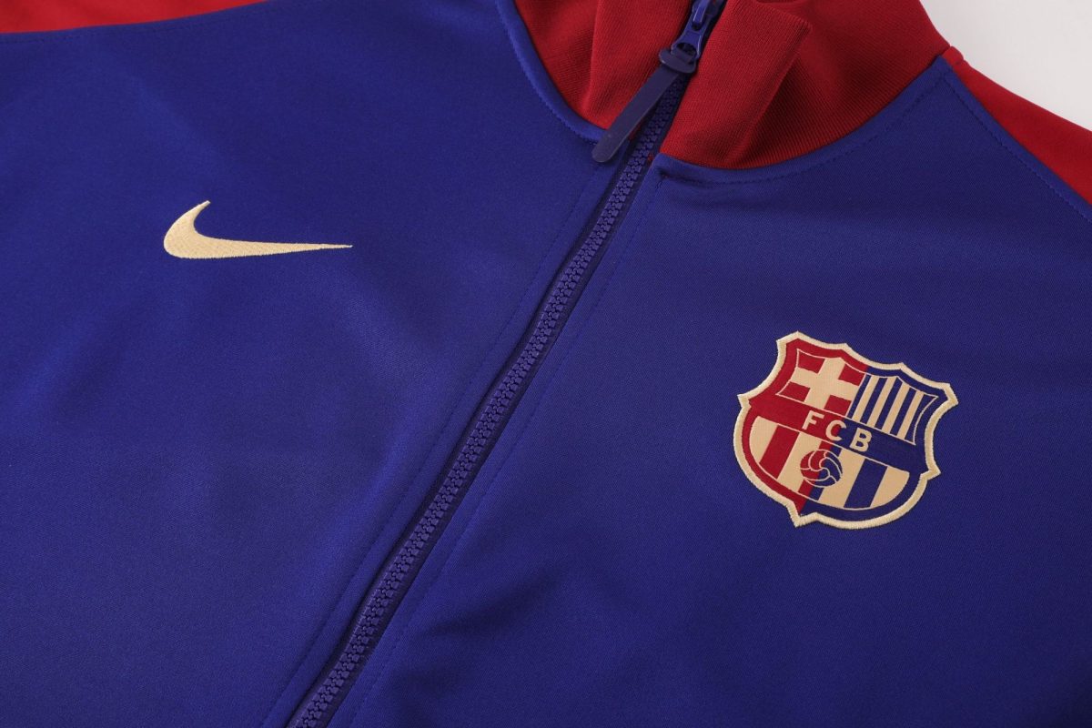 Close-up of a blue training jacket with a zipper, featuring a white Nike swoosh and the FC Barcelona crest on the chest area.