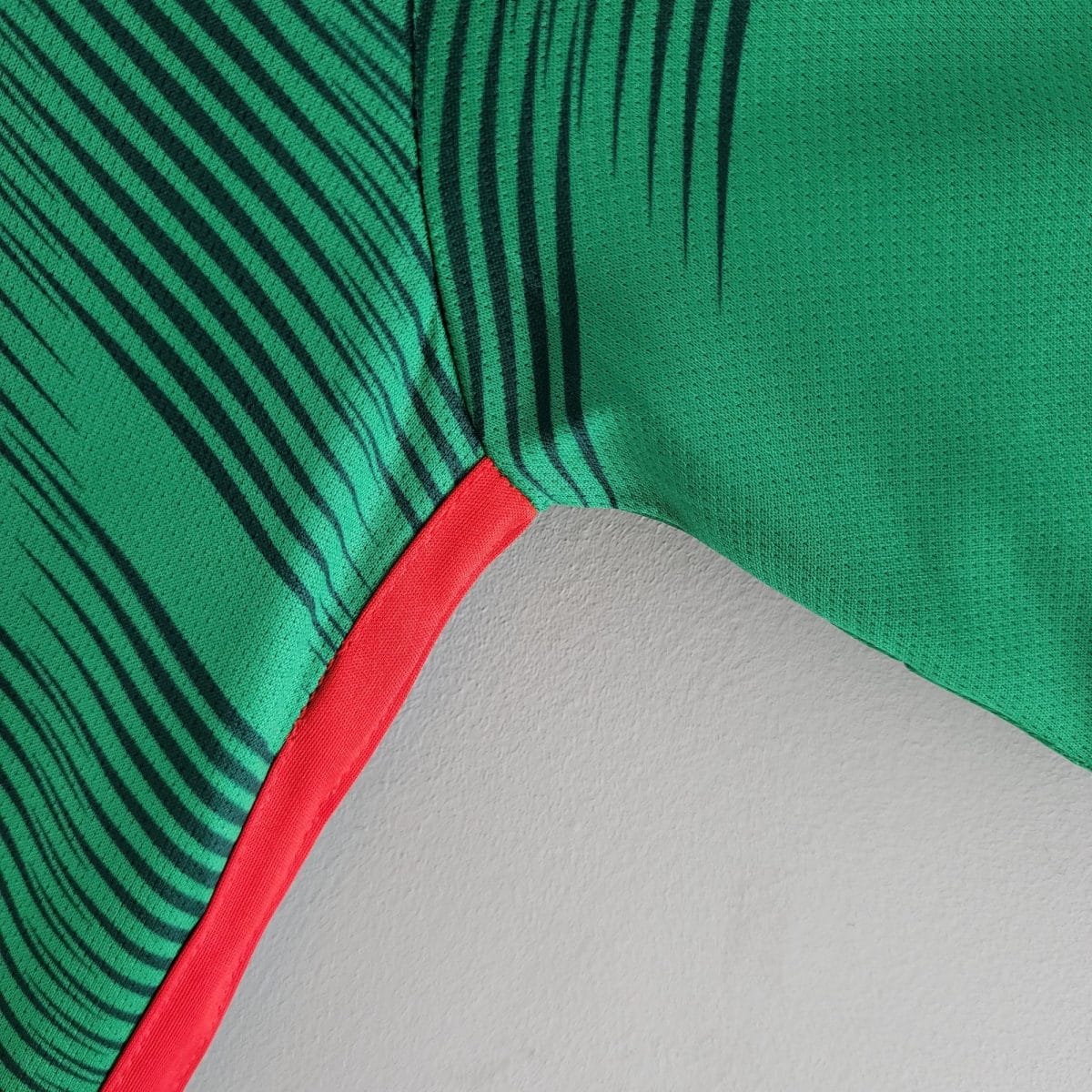 Close-up of green fabric with dark diagonal stripes and a red seam on a light gray background.