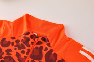 Bright orange zip-up jacket with a bold black abstract print and a high collar, shown from the chest area.