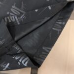 Close-up of black fabric with a repeated gray branded pattern, likely from a bag or jacket edge edge seam visible here