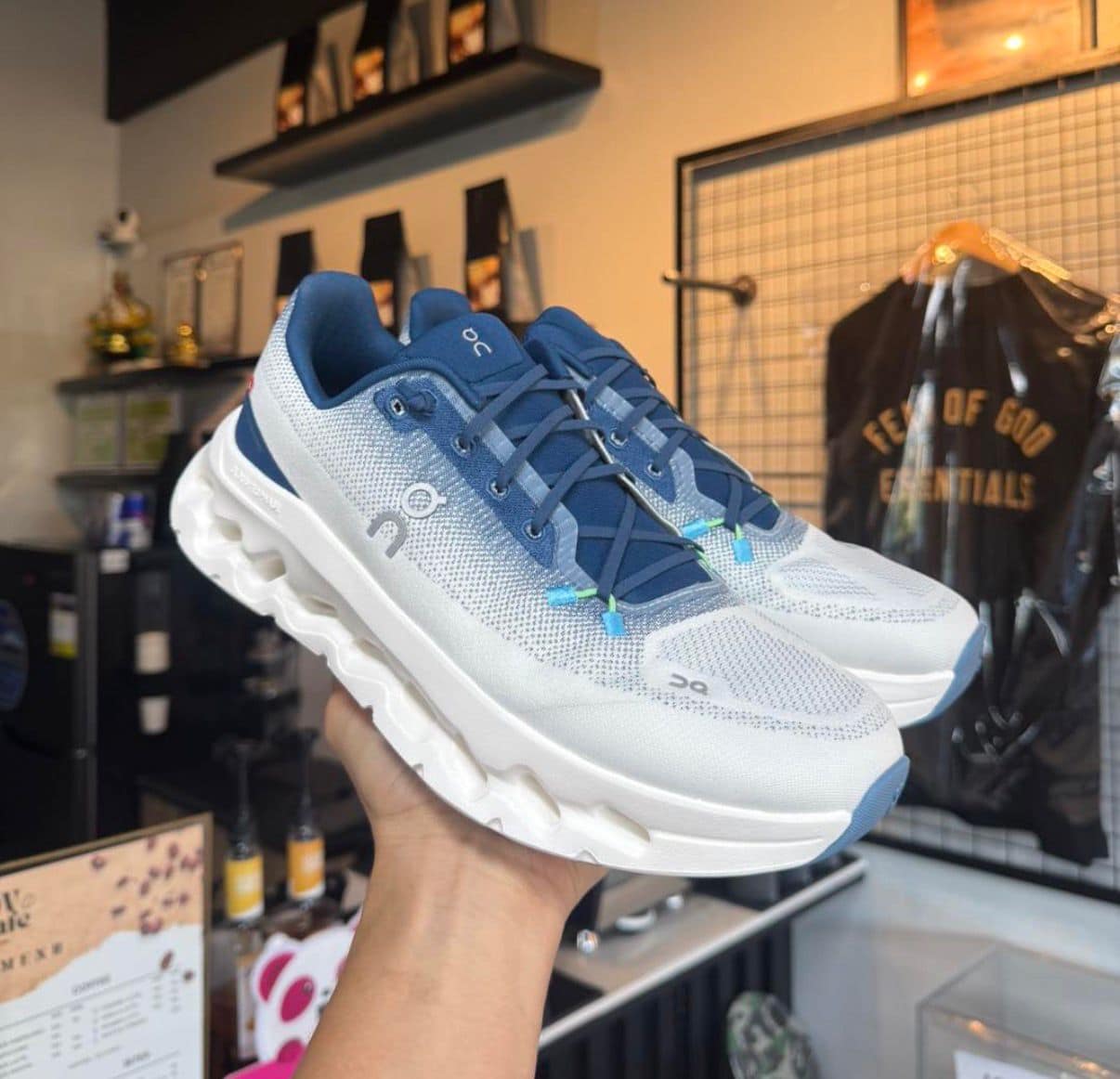 d665dc84-d8ac-462c-9193-906b221a9f88 | UAE SPORT STORE Pair of white and blue On running shoes being held up in a store, showing textured mesh upper and chunky sole.