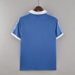 d67663cd_9052d643-4cf1-46e9-963b-acc756741d33 | UAE SPORT STORE Back view of a blue polo shirt on a wooden hanger, white collar and white cuff trim visible against a gray backdrop.