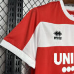 Red and white sports jersey hanging on a rack, showing the errea logo and partial bold white text on the chest.