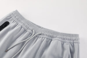 Close-up of light gray jogger pants waistband with drawstring and zip pocket similar detail visible near the left edge.
