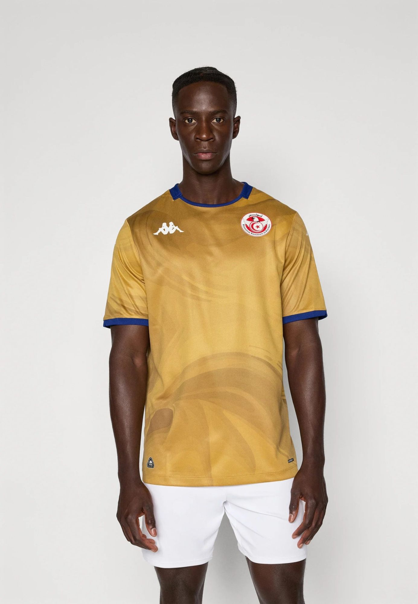 d7599b6e222d407db75a65e7fac8523e | UAE SPORT STORE Young man in a gold soccer jersey with blue trim and a circular crest on chest, standing against a light background.