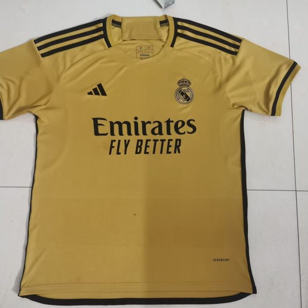 Yellow Real Madrid football jersey with black Adidas stripes on shoulders and Emirates sponsor text reading 'Emirates Fly Better' front and center.