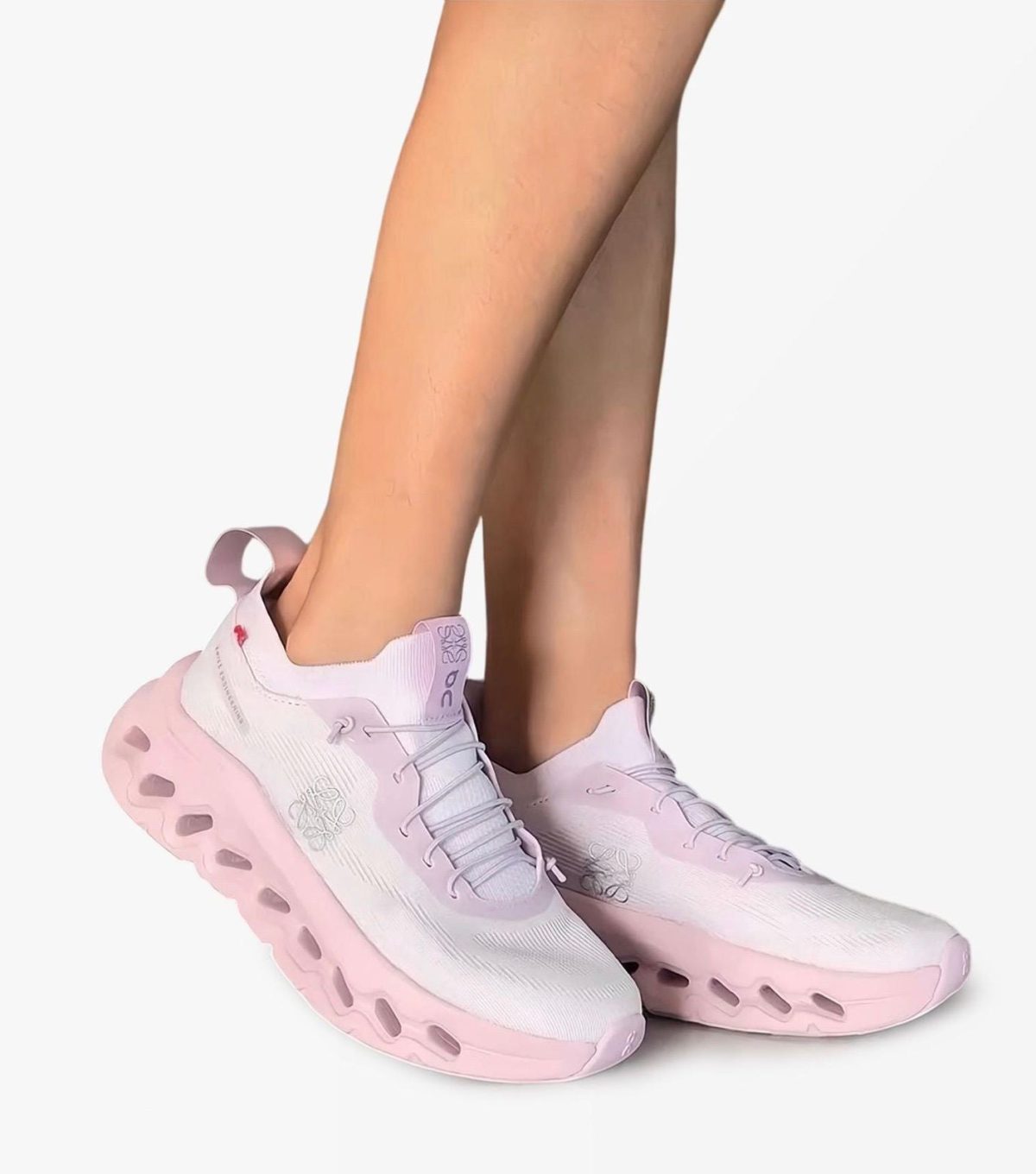 Close-up of pastel pink running shoes on a foot, white upper with a chunky pink sole showing cutouts from the side.