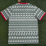 Short-sleeve shirt with a bold green tribal pattern over white, red sleeve cuffs, laid on grass.