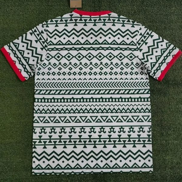 Short-sleeve shirt with a bold green tribal pattern over white, red sleeve cuffs, laid on grass.