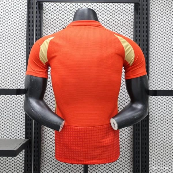 Back view of a red athletic jersey with gold shoulder panels on a display mannequin in a gym setting.