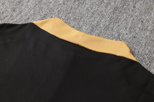 Close-up of black jacket with gold ribbed collar lying on gray carpet.