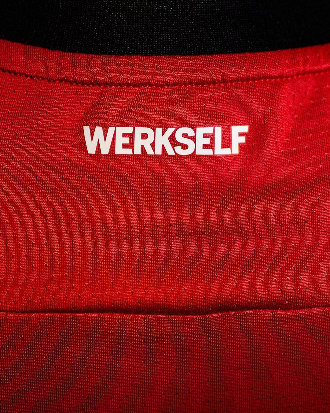 dHczHR65Orx3dK7 | UAE SPORT STORE Close-up of red sports jersey fabric with a white 'WERKSELF' logo across it.