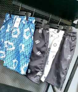 Blue patterned shorts with a Dior tag hanging on a clothing rack in a store window/aisle.