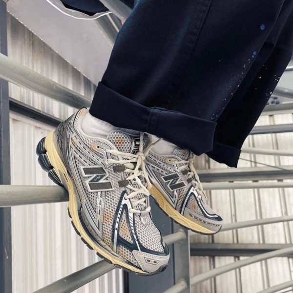 Gray and white sneakers resting on a metal railing with dark rolled-up pants nearby.