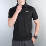 Torso of a person wearing a black Nike polo shirt with a white swoosh logo, hand at the collar, wearing a wristwatch visible.
