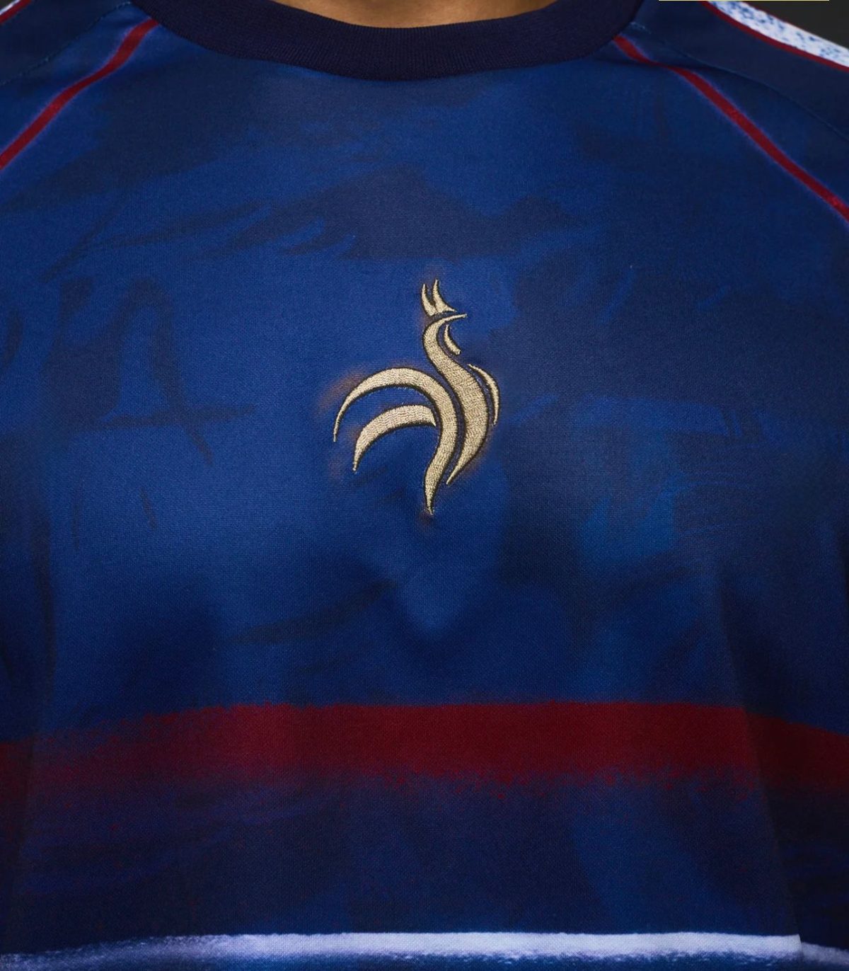 Blue sports jersey close-up showing a gold stylized rooster emblem on the chest area