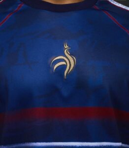 Blue sports jersey close-up showing a gold stylized rooster emblem on the chest area