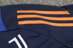 Navy sports jersey fabric with three orange wavy stripes across and a purple cuff, lying on a gray carpet.