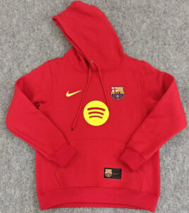 Red Barcelona hooded sweatshirt with a yellow Nike swoosh and Spotify logo on the front, display on a gray surface.