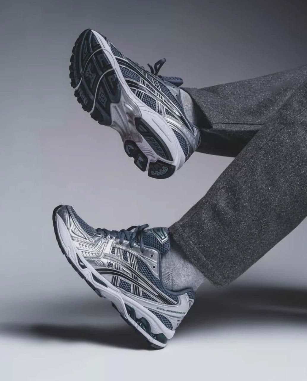 db87a82a-4d69-4e23-a183-eabb92b149a9 | UAE SPORT STORE Two gray and white running shoes suspended mid-air as if kicked up in a jump against a neutral background.